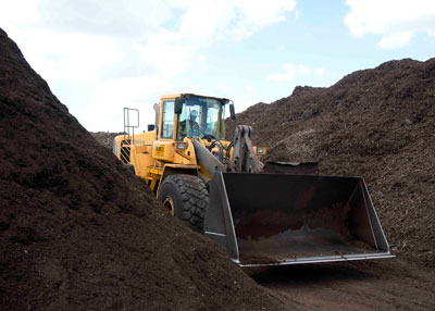Front-end loader is being used to blend composted organic matter in background into a planting mix.